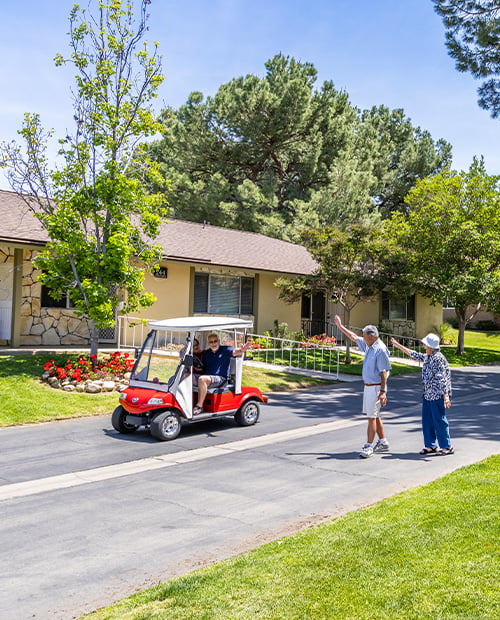 two seniors waving at another senior in red golf cart