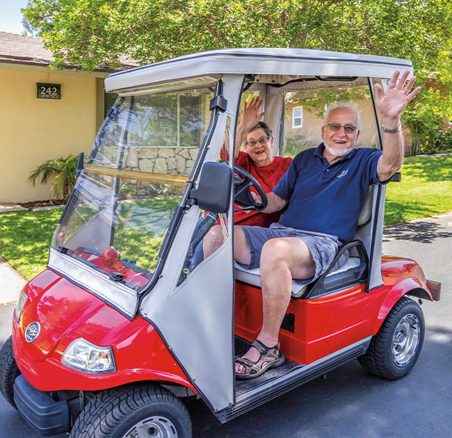 two seniors waving in red gold cart