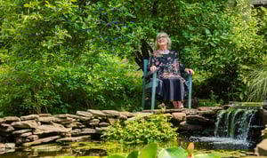 senior sitting in chair next to a pond with a small waterfall