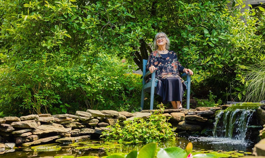 senior sitting in chair next to a pond with a small waterfall