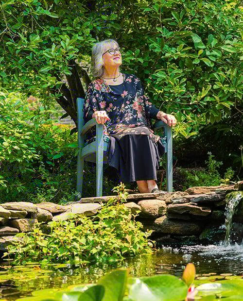 senior sitting on a chair next to a pond with a small waterfall