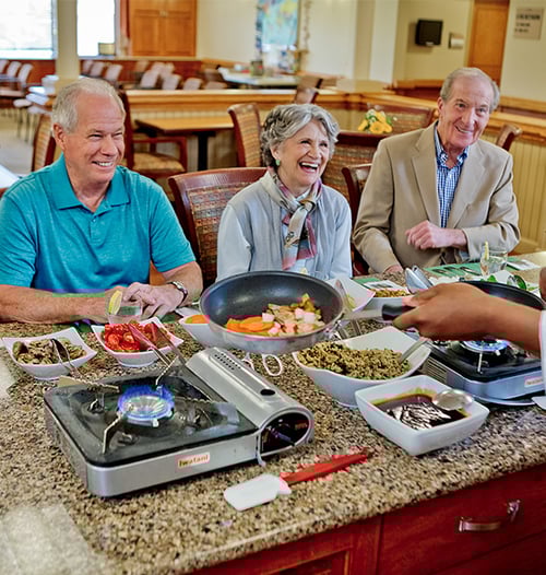 seniors enjoying a meal that is freshly prepared in front of them by a chef